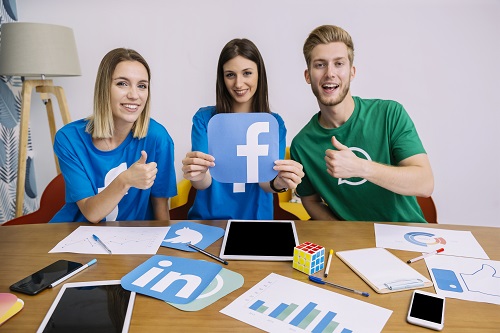 smiling-woman-holding-facebook-logo-with-his-friends-showing-thumbup-sign